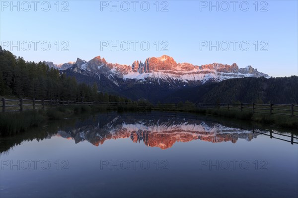 The sunset bathes the mountain peaks in warm light that is reflected in the lake, Trentino-Alto Adige, Alto Adige, Bolzano province, Dolomites, Reflection rose garden at Wuhnleger Lake, San Cipriano