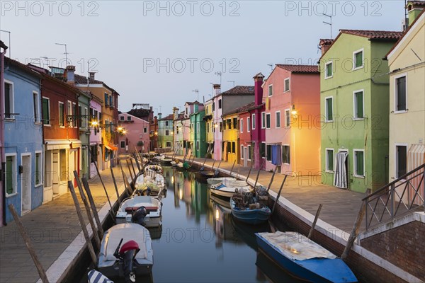 Moored boats on canal lined with colourful stucco houses, shops and footbridge at dusk, Burano Island, Venetian Lagoon, Venice, Veneto, Italy, Europe