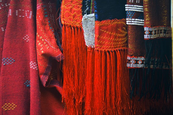 Close-up of traditional Ulos clothes of the Batak people with fringe and intricate indigenous patterns hanged in a row, displayed for sale in the local market. Samosir, North Sumatra Indonesia