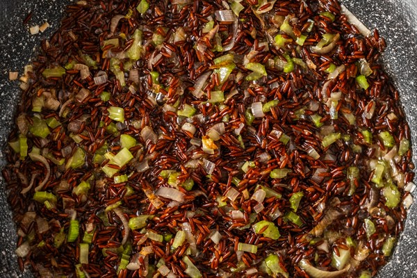 Closeup top view of frying pan with pink rice, onion and celery