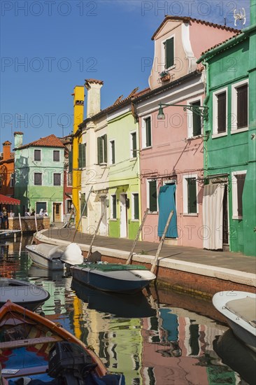 Moored boats on canal lined with pink, yellow and green stucco houses decorated with striped curtains over entrance doors, Burano Island, Venetian Lagoon, Venice, Veneto, Italy, Europe