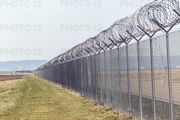 A long security fence with barbed wire in a field under a clear sky