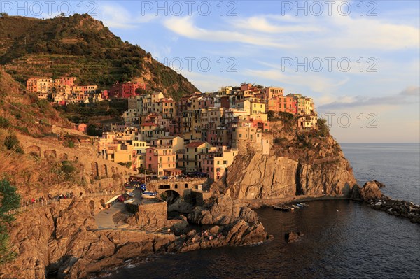 Morning sun shines on a colourful coastal town on the Italian Riviera with a view of the calm sea, Italy, Liguria, Manarola, Riomaggiore, La Spezia Province, Cinque Terre, Europe