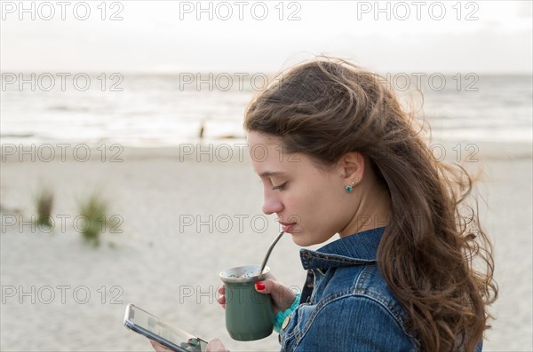 Beautiful young woman drinking Chimarao, mate tea tea (yerba mate tea tea infusion drink) on the beach in Uruguay