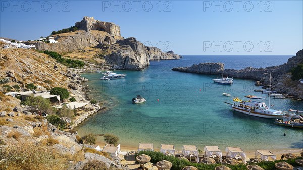 Sunny beach day with a view of a bay, cliffs and parked boats, Paulus Bay, below the Acropolis of Lindos, Lindos, Rhodes, Dodecanese, Greek Islands, Greece, Europe