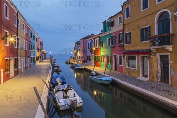 Moored boats on canal lined with colourful stucco houses and shops at dusk, Burano Island, Venetian Lagoon, Venice, Veneto, Italy, Europe