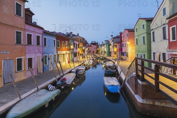 Moored boats on canal lined with colourful stucco houses, shops and footbridge at dusk, Burano Island, Venetian Lagoon, Venice, Veneto, Italy, Europe