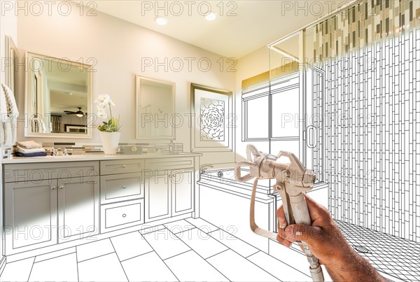 Professional spray painter holding spray gun spraying renovated bathroom over design drawing