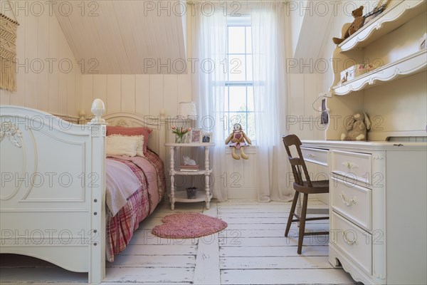 Single bed with red, pink and grey tartan bedspread, white painted antique style wooden headboard and footboard, nightstand, dresser with brown chair in a kid's bedroom with white painted larch wood floorboards on upstairs floor inside country style home, Quebec, Canada, North America