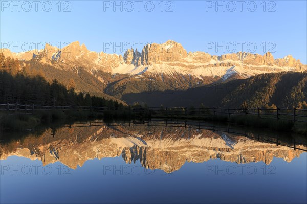 Sunrise behind the mountains with bright red colours reflected in the clear water of the lake, Trentino-Alto Adige, Alto Adige, Bolzano province, Dolomites, Reflection rose garden at Wuhnleger Lake, San Cipriano