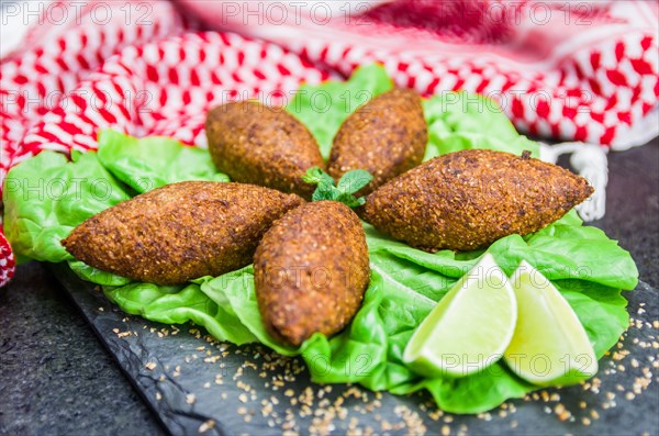 Delicious Lebanese (Arabic) food, kibbeh (kibe) with sauces and lemon on black slate stone and granite background with traditional keffyeh