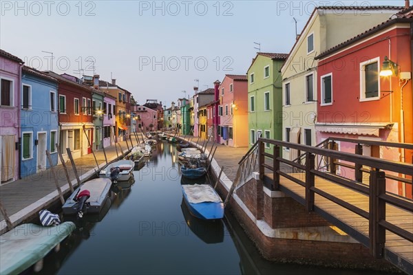 Moored boats on canal lined with colourful stucco houses, shops and footbridge at dusk, Burano Island, Venetian Lagoon, Venice, Veneto, Italy, Europe