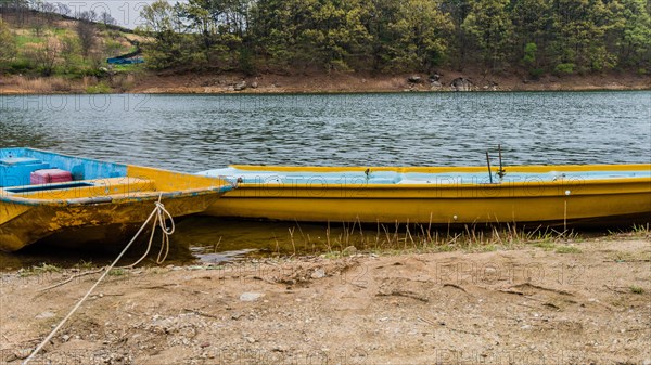 Two yellow metal boats tied up at the shore of a peaceful lake with trees on the far shoreline in South Korea