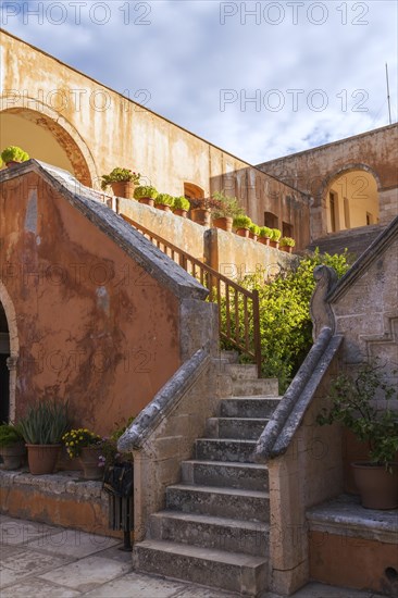 Stone staircase leading to cloister and wall with various plants in terracotta planters in inner courtyard at Holy Trinity (Agia Triada) Monastery, Akrotiri Peninsula, Chania region, Crete Island, Greece, Europe