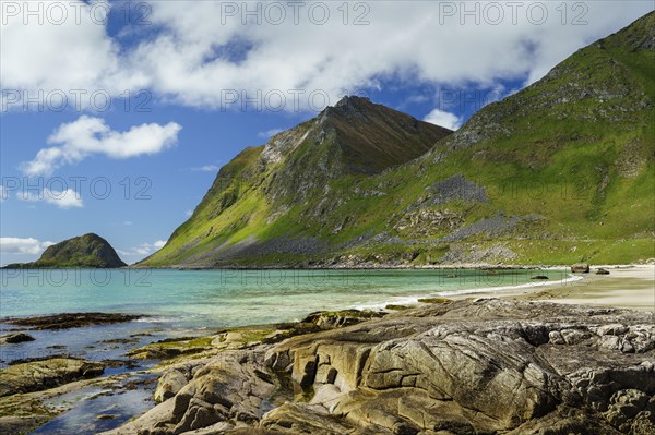 Landscape with sea at the sandy beach of Haukland (Hauklandstranda) with the mountain Veggen. Rocks in the foreground. Shot during the day with blue sky. Early summer. Haukland Beach, Haukland, Vestvagoya, Lofoten, Norway, Europe