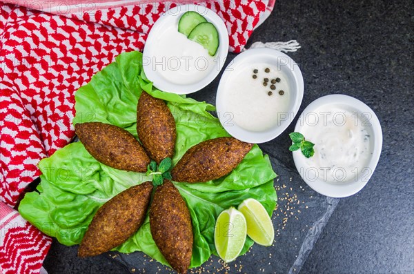 Delicious Lebanese (Arabic) food, kibbeh (kibe) with sauces and lemon on black slate stone and granite background with traditional keffyeh