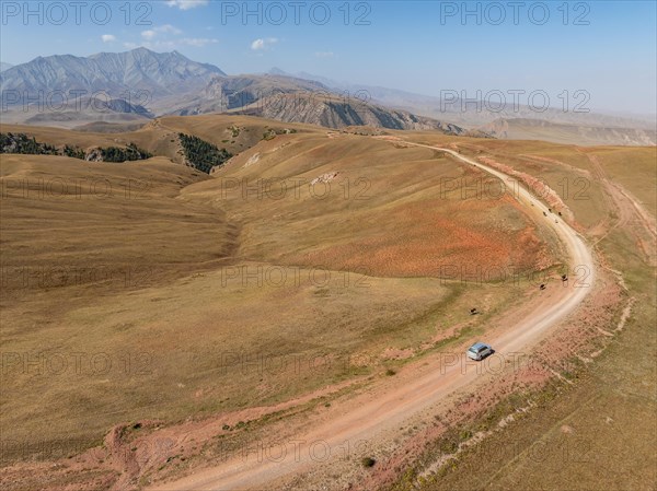 Moldo-Ashuu Pass, car on road between yellow hills, near Baetov, Naryn region, Kyrgyzstan, Asia