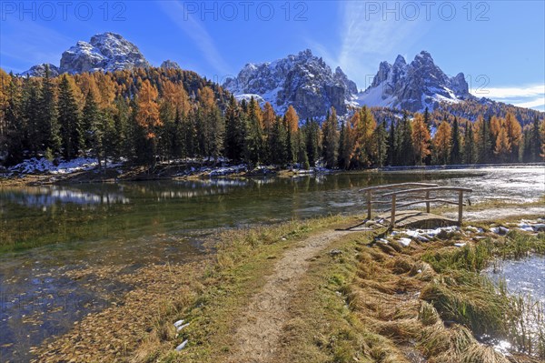 A hiking trail leads to a quiet lake surrounded by autumnal trees and mountains, Italy, South Tyrol, Belluno, Dolomites, Lago d'Antorno against Cadini, Misurina, Sesto Dolomites, Veneto, Europe