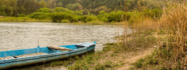 Landscape of wooded area around a small lake with a blue wooden boat anchored at shore in South Korea
