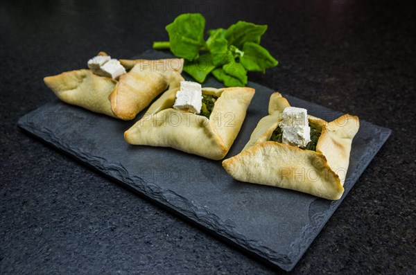 Delicious Lebanese (Arabic) food, spinach sfiha with ricotta cheese on black stone background