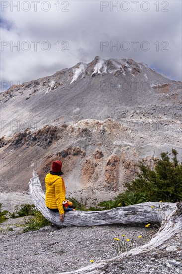 Young woman in yellow jacket sits in front of a volcano, Chaiten Volcano, Carretara Austral, Chile, South America