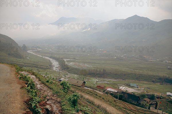 A misty view of a village in a valley with a river flowing through, surrounded by mountains in Lao Cai Village, Sa pa Vietnam