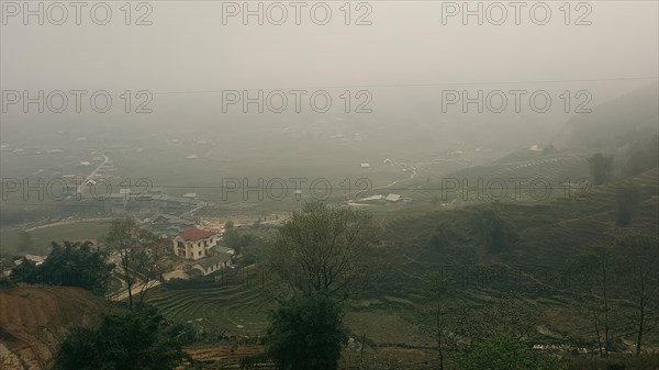 A foggy rural landscape with terraced fields and a singular house amidst greenery in Lao Cai Village in Sa pa, Vietnam, Asia