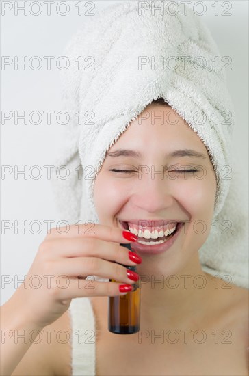 Happy young woman with towel on head holding amber glass bottle of skin serum. Beautiful young Brazilian woman moisturizes her skin with serum isolated against white background