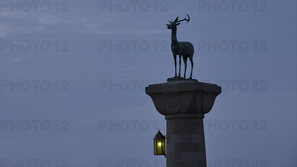 Deer statue on column with illuminated lantern at dusk, Mandraki Oat, Rhodes, Dodecanese, Greek Islands, Greece, Europe