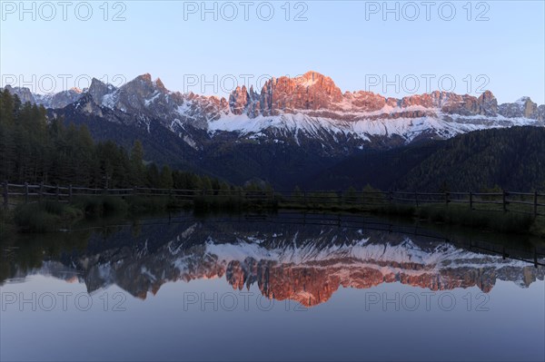 Early morning light illuminates a mountain range reflected in a still lake, Trentino-Alto Adige, Alto Adige, Bolzano province, Dolomites, Reflection rose garden at Wuhnleger Lake, San Cipriano