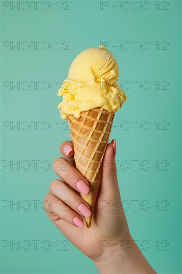 Hand holding yellow ice cream in cone in front of green studio background. KI generiert, generiert, AI generated