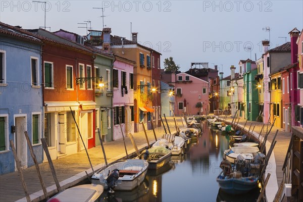 Moored boats on canal lined with colourful stucco houses and shops at dusk, Burano Island, Venetian Lagoon, Venice, Veneto, Italy, Europe