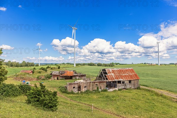 Old ruined farm in a rural landscape view with wind turbines on the fields in the summer, Sweden, Europe