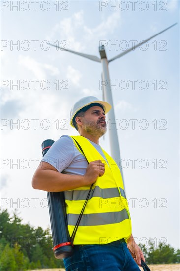 Vertical photo of the profile of a male mautre caucasian worker with protective gear and drawing tube in a green energy park next to a wind turbine