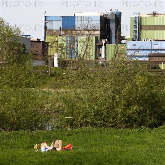 Couple lies on the Ruhrauen in front of the stainless steel plant in Witten, Ruhr area, North Rhine-Westphalia, Germany, Europe