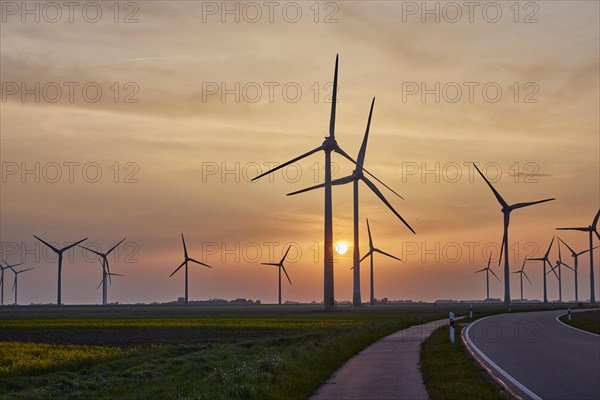 Wind turbines with country road and cycle path in front of setting sun and sunset near Bordelum, Nordfriesland district, Schleswig-Holstein, Germany, Europe