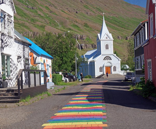 Small church and houses line a street decorated with rainbow colours, Seydisfjoerdur. Iceland