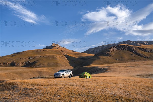 All-terrain vehicle Toyota Land Cruiser and green camping tent in the Kyrgyz highlands, hills with yellow grass, Sary Jaz valley, Tien Shan, Kyrgyzstan, Asia