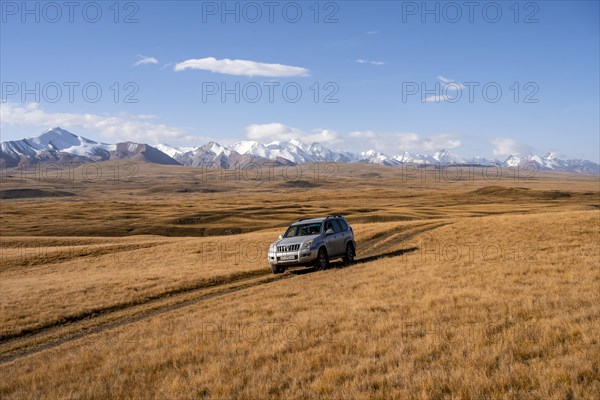 Off-road vehicle Toyota Land Cruiser driving on a track through yellow grass, behind glaciated mountain peaks of the Tien Shan Mountains, Sary Jaz Valley, Kyrgyzstan, Asia