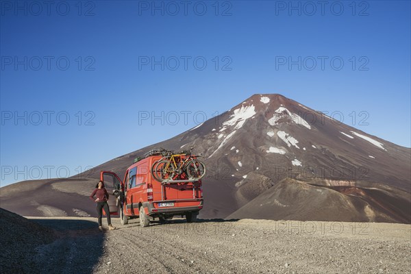 Young woman and her campervan in front of the Lonquimay volcano, Lonquimay volcano, Malalcahuello National Reserve, Curacautin, Araucania, Chile, South America