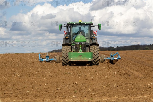 Green John Deere tractor ploughing deep furrows to prepare soil for potato crop, Ramsholt, Suffolk, England, UK