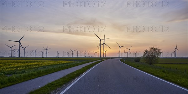 Wind turbines with country road and cycle path in front of setting sun and sunset near Bordelum, Nordfriesland district, Schleswig-Holstein, Germany, Europe