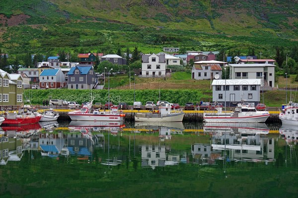 Fishing boats and houses reflected in the calm waters of a fjord, East Iceland, Seydisfjoerdur, Iceland, Europe
