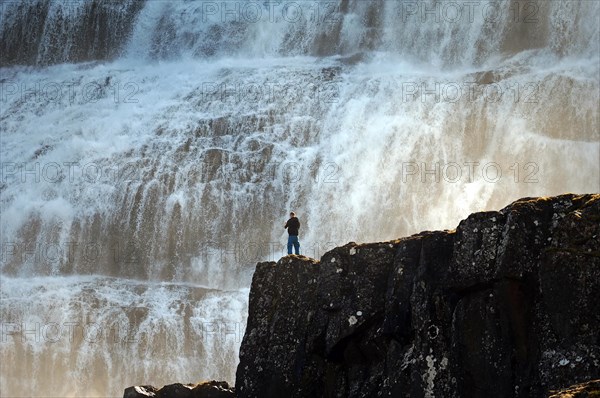 Man standing on a rock in front of the falling water of a waterfall, Dyandi, Westfjords, Iceland, Europe