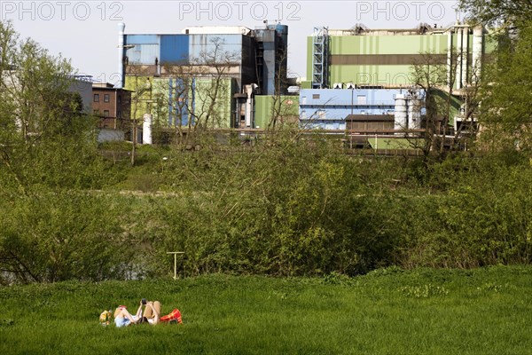 Couple lies on the Ruhrauen in front of the stainless steel plant in Witten, Ruhr area, North Rhine-Westphalia, Germany, Europe