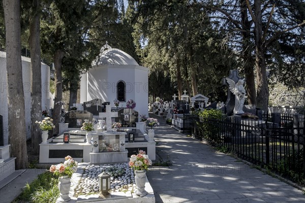 A white chapel surrounded by tombstones and an angel statue in a peaceful cemetery, Lindos, Rhodes, Dodecanese archipelago, Greek Islands, Greece, Europe