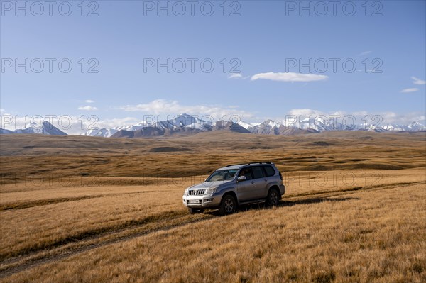 Off-road vehicle Toyota Land Cruiser driving on a track through yellow grass, behind glaciated mountain peaks of the Tien Shan Mountains, Sary Jaz Valley, Kyrgyzstan, Asia