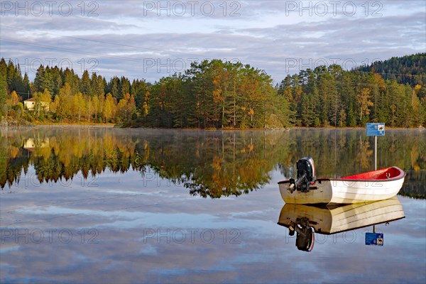 Trees and a small boat reflected in the calm waters of a lake, leaf colouring, Bullaren, Bohuslaen. Sweden