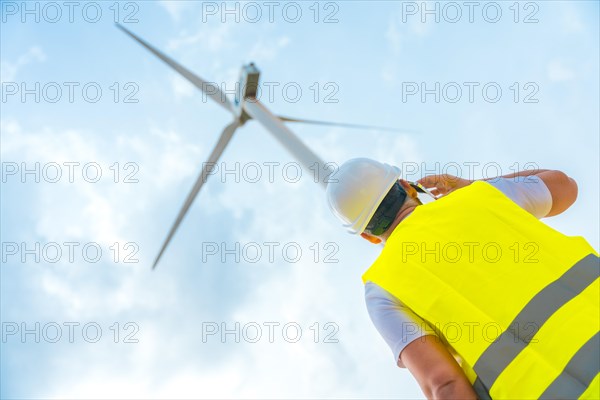 Low angle view photo of a male caucasian adult Engineer using phone next to a wind turbine in a green energy park