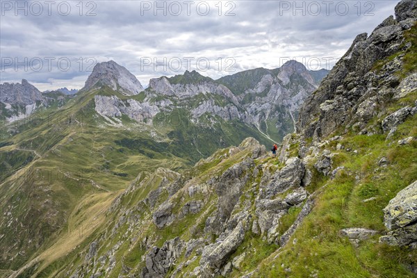 Mountaineer on a narrow hiking trail on a steep meadow slope, descent from the Raudenspitze, view into the Val Fleons valley with rocky mountain peaks, Carnic Main Ridge, Carnic Alps, Carinthia, Austria, Europe